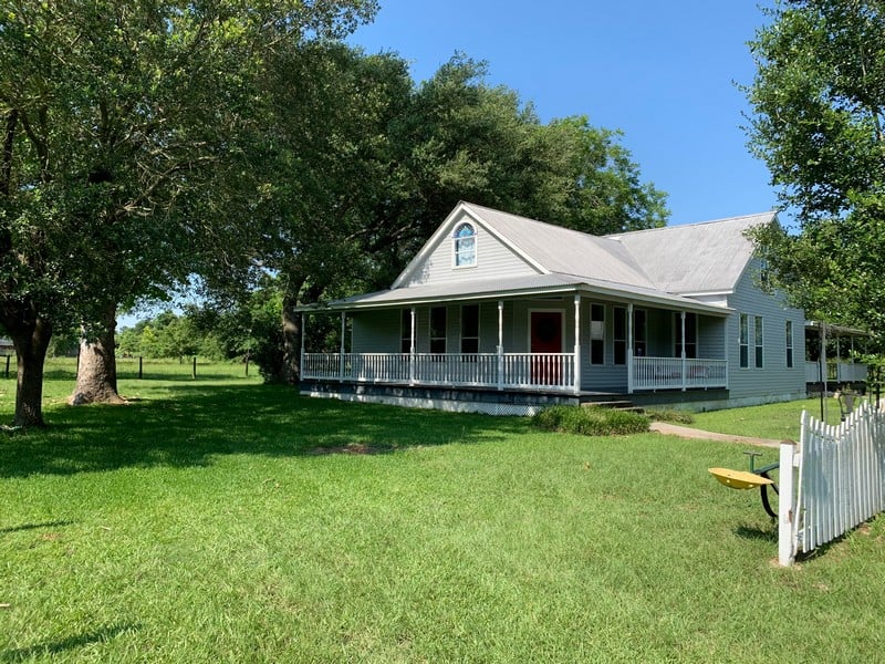 White house with porch and large trees in yard.