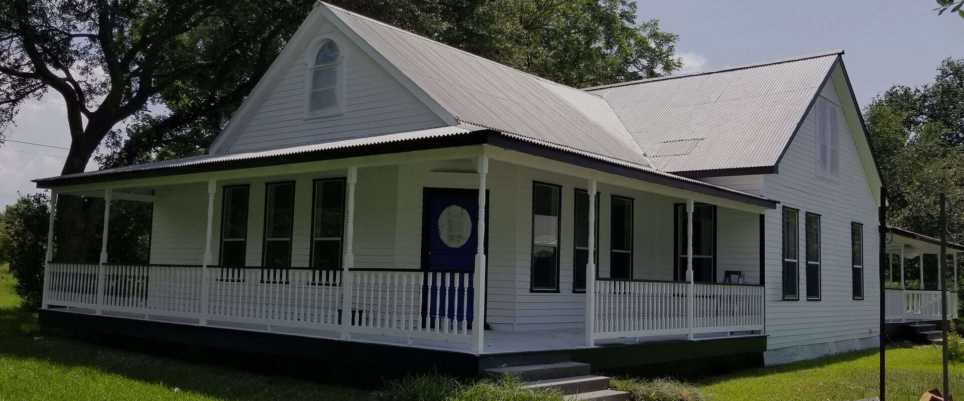 White house with wraparound porch and gabled roof.